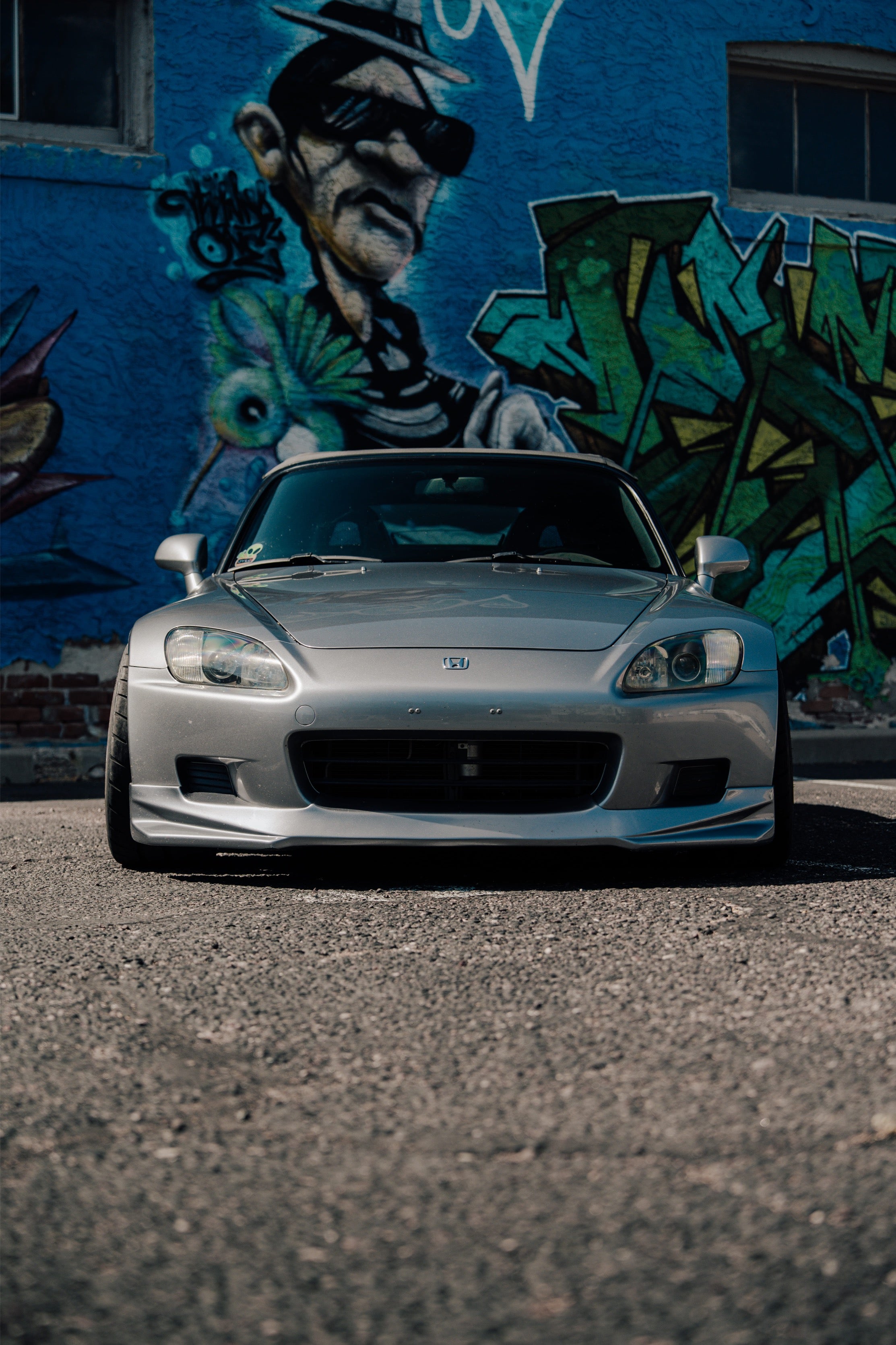 Silver Honda S2000 parked in front of a graffiti wall