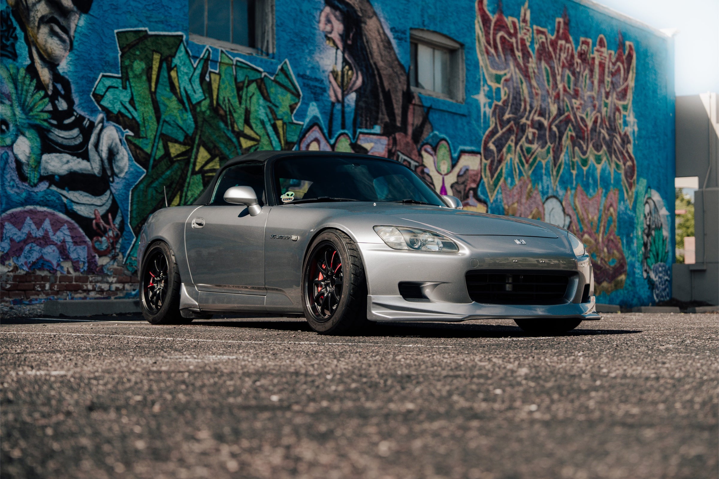 Silver Honda S2000 parked in front of a graffiti wall